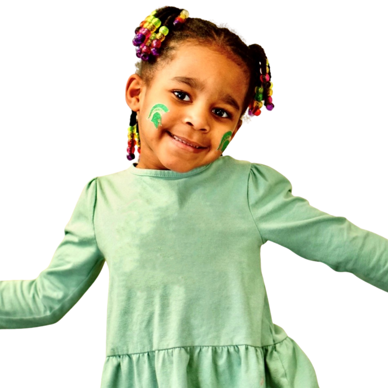A little girl strikes a cheer pose, sporting a glittery green Spartan helmet sticker on each cheek.