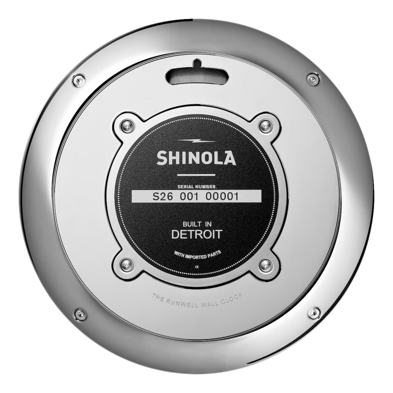The back of a chrome clock with green face and white lettering. Shinola Detroit displayed under the 12 and a Spartan helment in the place of the 6. White lettering for the hours and minutes, with chrome sweeping hands.