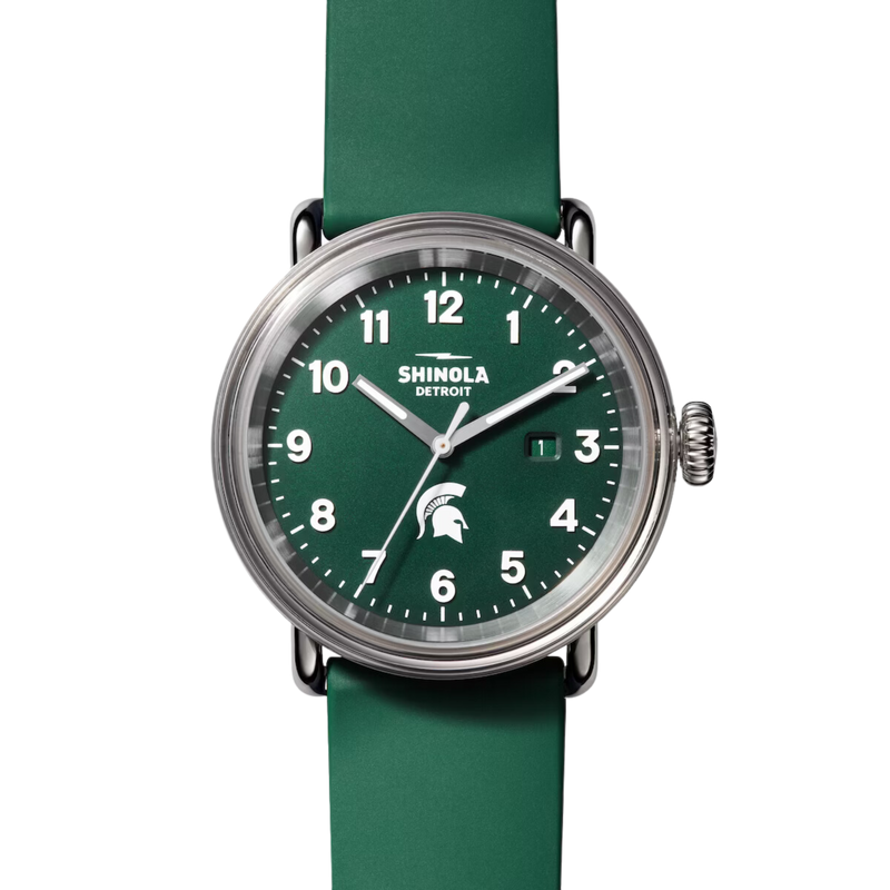 Chrome watch with green face and white lettering. Shinola Detroit displayed under the 12 and a Spartan helmet above the 6. White lettering for the hours and minutes, with chrome sweeping hands, and a forest green silicone band.