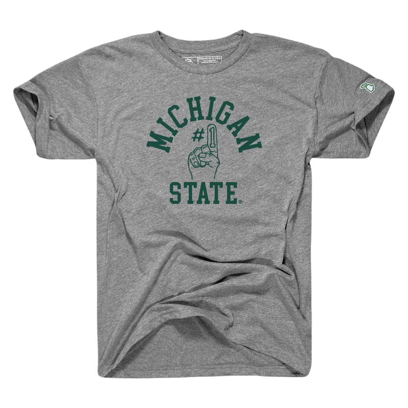 A gray tee shirt with the words Michigan State written in green on the center torso. In the middle of the two words, a graphic of a foam finger with