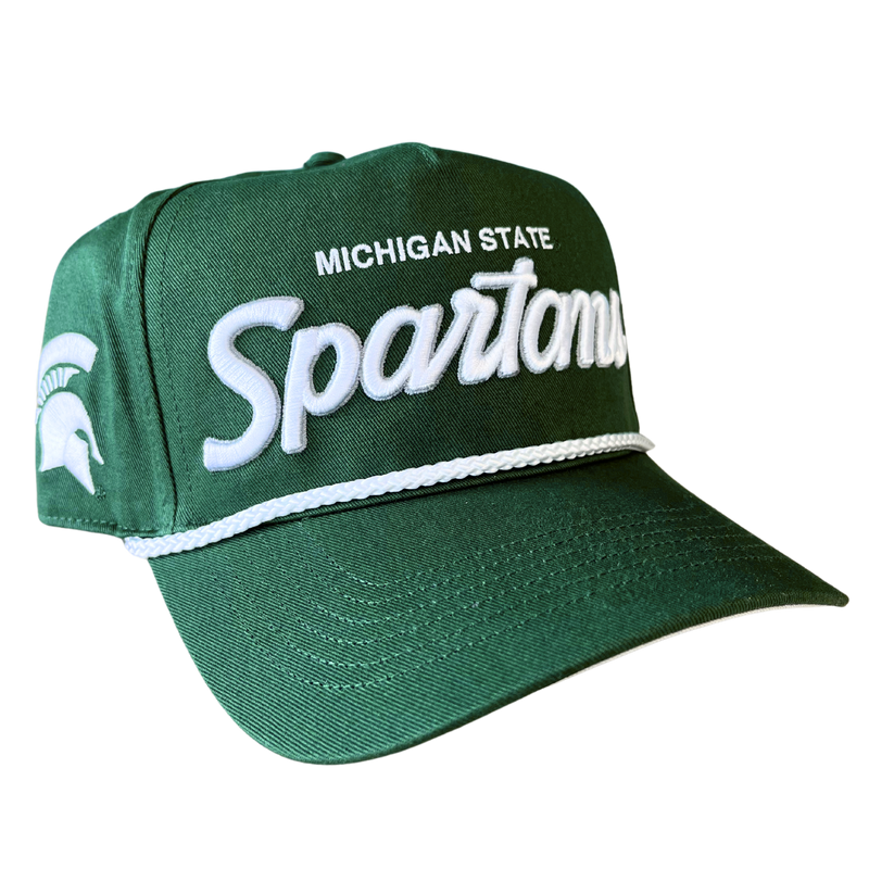 An angled view of a green baseball cap with Michigan State embroidered in white above an embroidered stylized script reading “Spartans” in white with a silver outline. Embroidered on the right temple panel is a white Spartan helmet. Over the bill is a white braided cord.