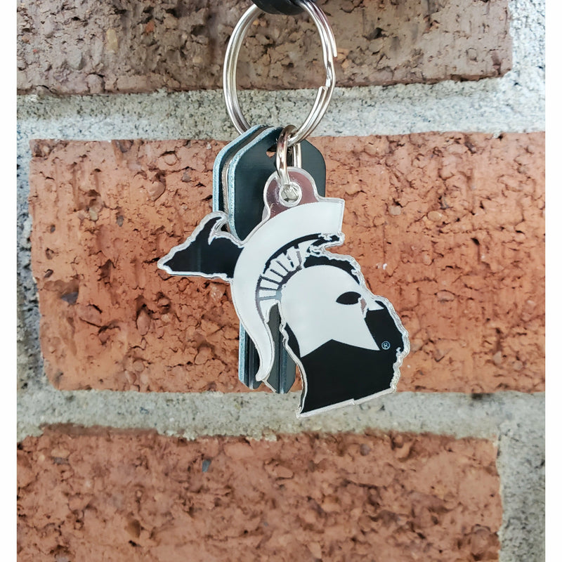 Closeup of the acrylic keychain and keyring with 3 silver and dark green keys against a brick wall. The acrylic piece hangs past the length of the 3 house keys