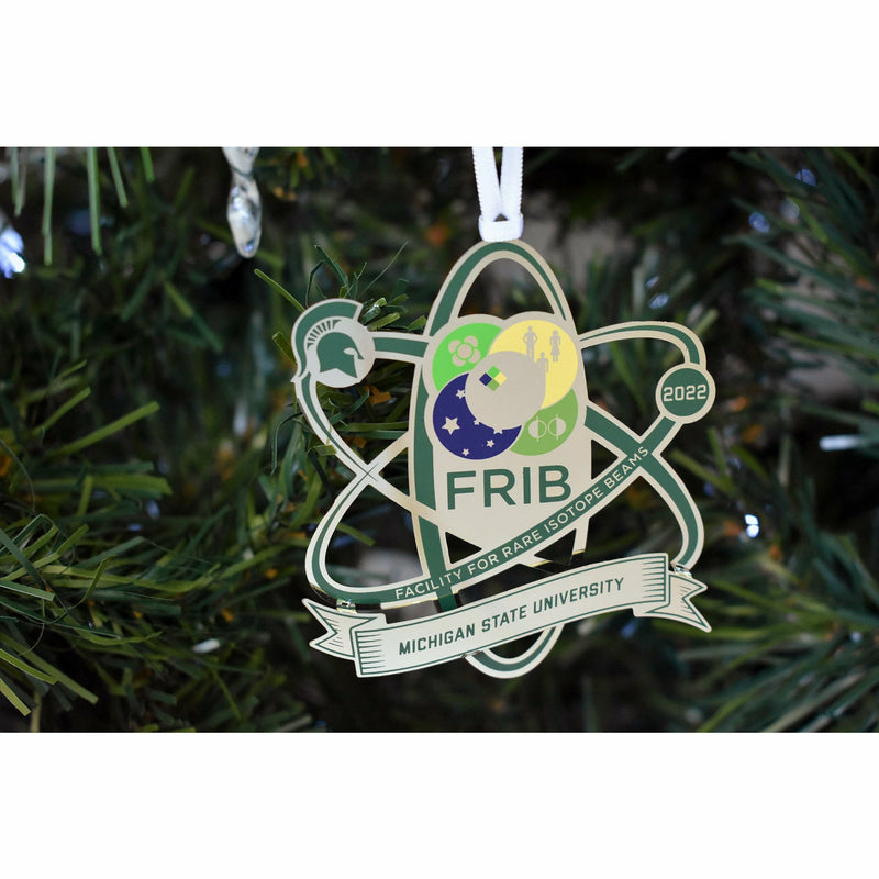Front photo of the silver FRIB 2022 Michigan State University ornament hanging in a decorated holiday tree.