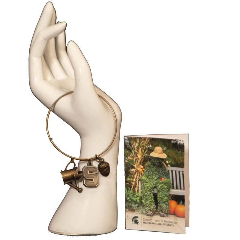 The bronze "the listener" bracelet on a hand mannequin next to a greeting card featuring a photo of Bernie (a screcrow type man made out of plants on a bench) in autumn.