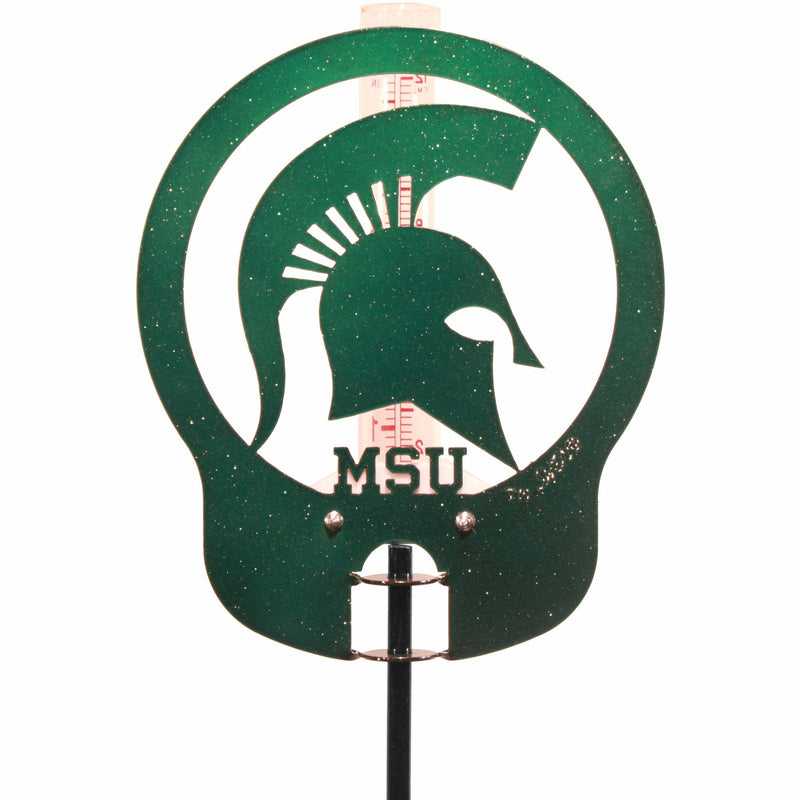 Close-up of the green metal cut-out in a circular shape with a Spartan helmet and small block letters reading MSU. The metal plate covers the rain gauge from the front.
