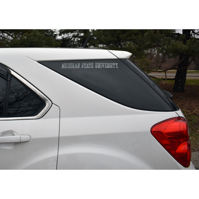 Rear window of a white SUV with the Michigan State University letter stickers placed
