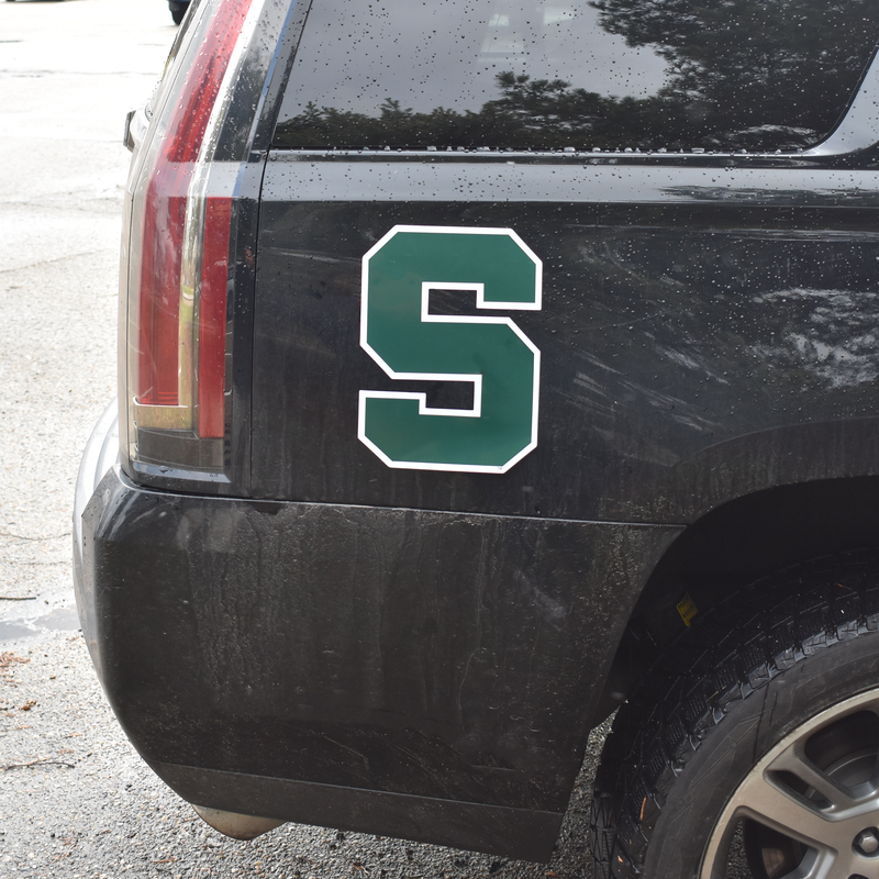 A large magnetic Spartan block S decal is affixed to the rear passenger side of a black SUV.
