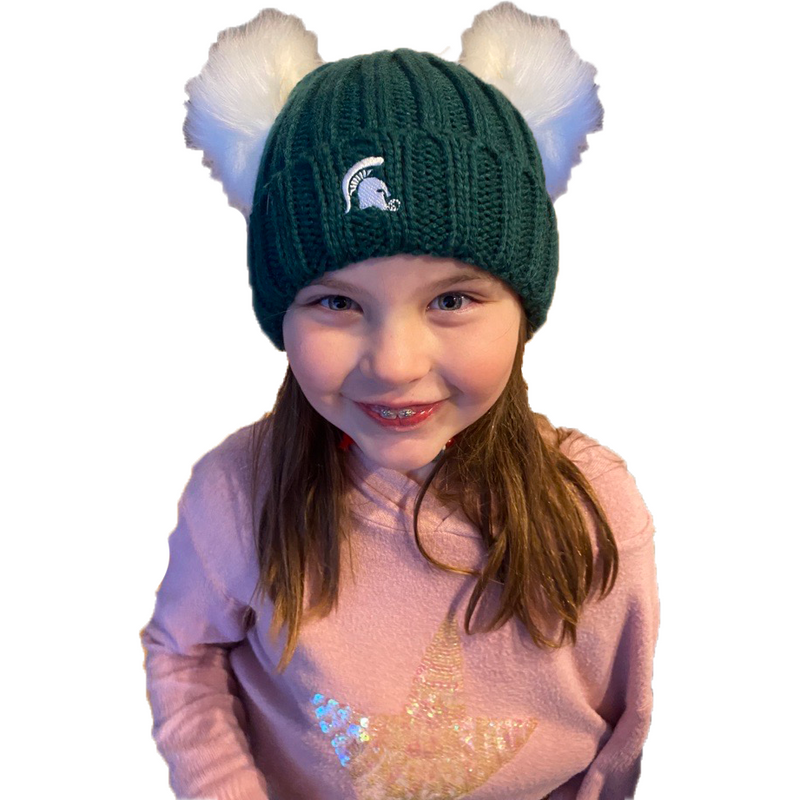 A girl wearing a green beanie with white pom knits. The MSU spartan helmet logo is placed in the front of the beanie in white. 