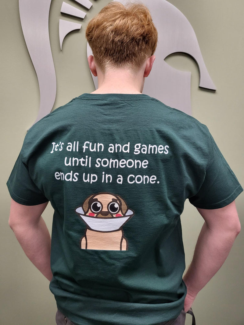 Person in green t-shirt standing backwards. Back of t-shirt that printed in white with "It's all fun and games until someone ends up in a cone." with an animated dog with a cone on below. 