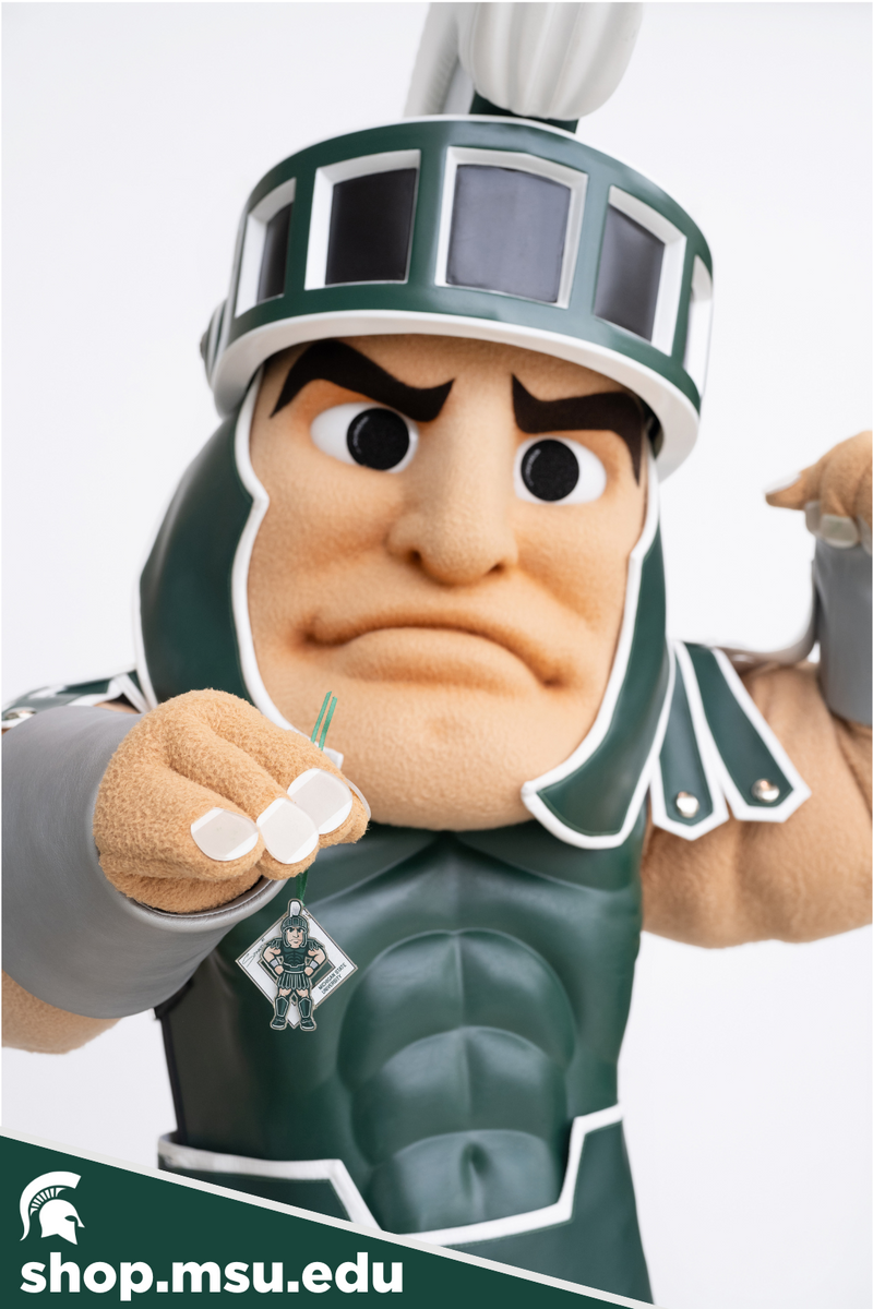 Sparty holding the 2024 Sparty Signature Collectible in one hand while flexing the other arm. The collectible features a figure of Sparty with his hands on his hips in front of a diamond-shaped white background.