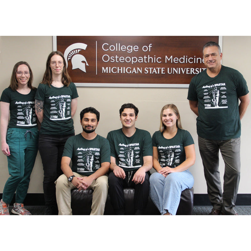 A group of six Radiology faculty, staff, and students model the Anatomy of a Spartan t-shirt in front of a College of Osteopathic Medicine sign.