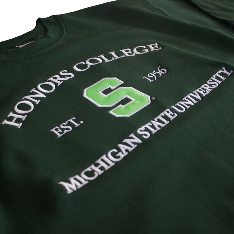 Crewneck sweatshirt in the deep forest. Across the chest are three lines of white text with an embroidered “Honors College”, “Est. 1956”, and “Michigan State University”. Between “Est.” and “1956” is a large block S in lime green.    