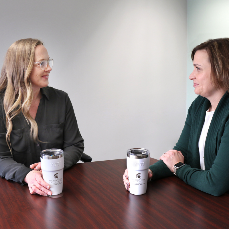 Two people sitting at a table with two white engraved MSU College of Osteopathic Medicine Yeti tumblers. 