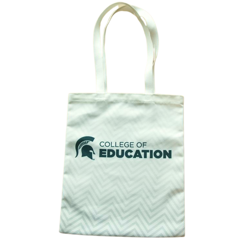 A white canvas tote with a chevron design and green College of Education logo and Spartan helmet. The chevron design fades from a darker gray at the bottom to a lighter gray at the top.