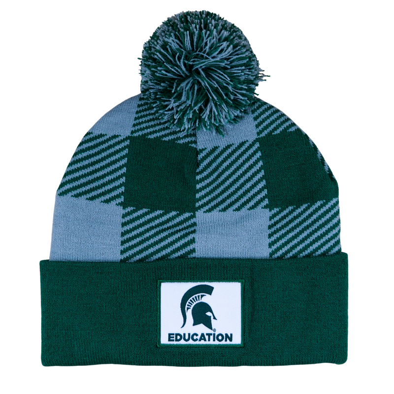 A green and gray plaid beanie with a matching pom. The cuff of the hat is an MSU green with a white sewn patch that features the MSU helmet with "Education" in green.