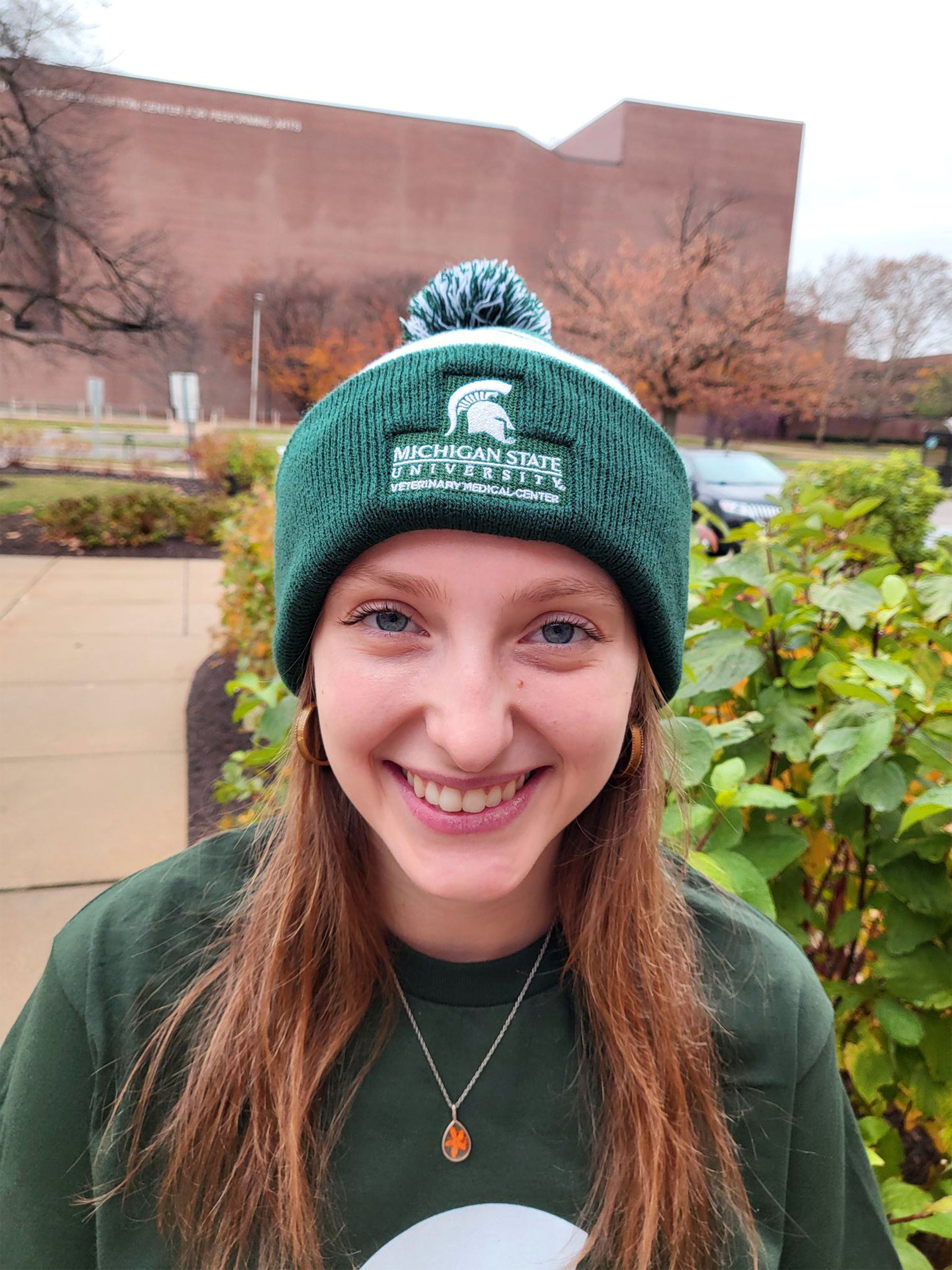 A woman in green T-shirt wearing a green and white striped beanie. The beanie is embroidered with a Veterinary Medical Center logo in white.