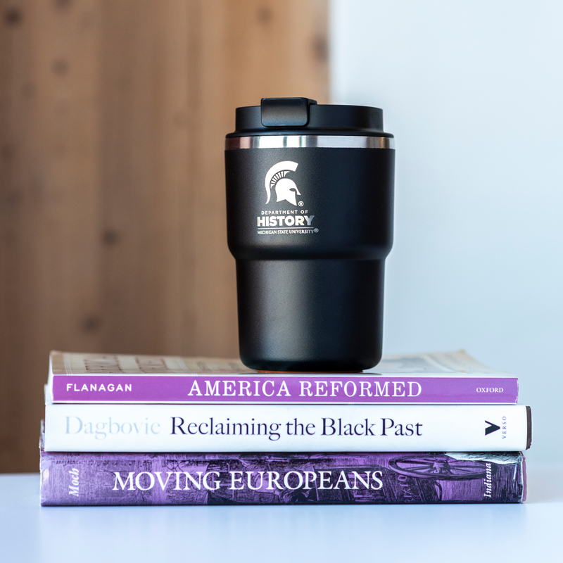 A black 12oz mug with a laser-etched Department of History logo and Spartan helmet sitting on top of 3 books. 