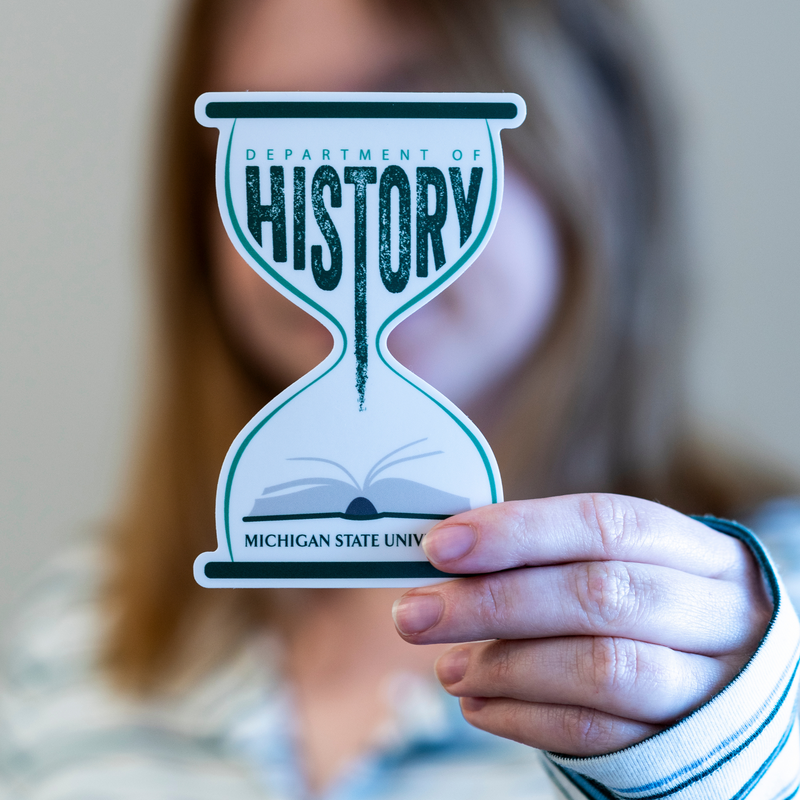 Person holding a forest green and white vinyl sticker that features an hourglass, history book, and the text “Department of History”. 