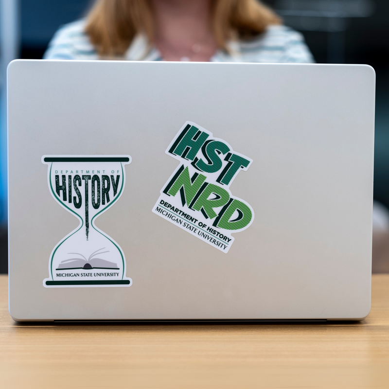 Two stickers on a laptop. Forest green and white vinyl sticker that features an hourglass, history book, and the text “department of history”. 