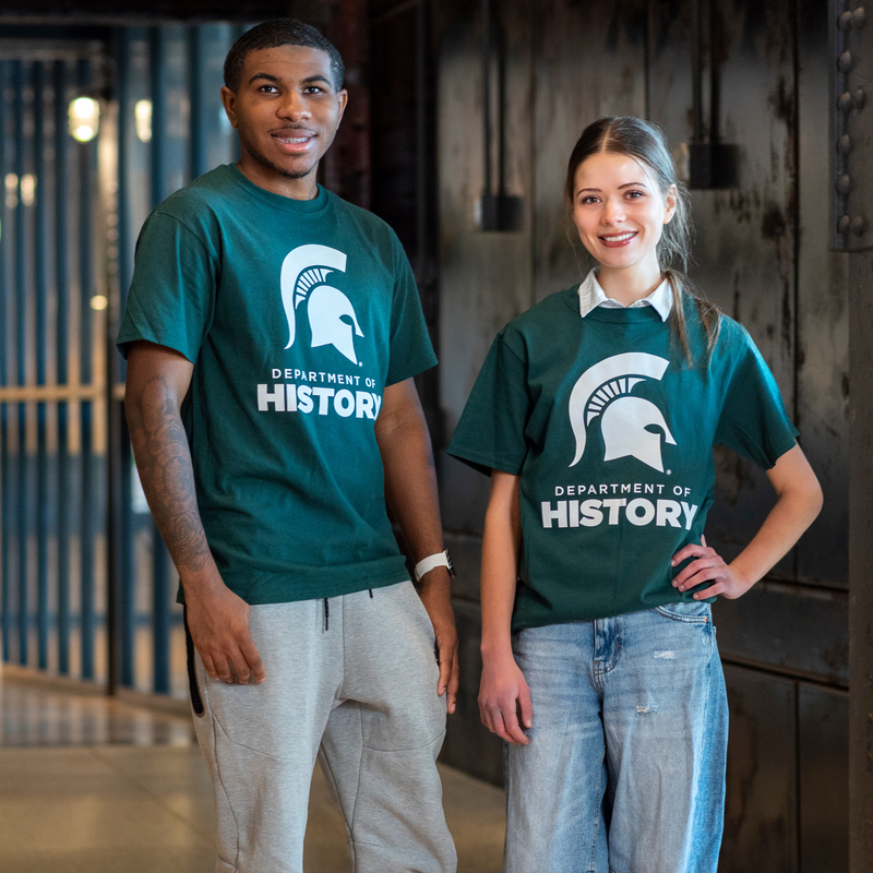 Two individuals wearing forest green T-shirts featuring the Spartan helmet above the text ‘Department of History’ printed in white.