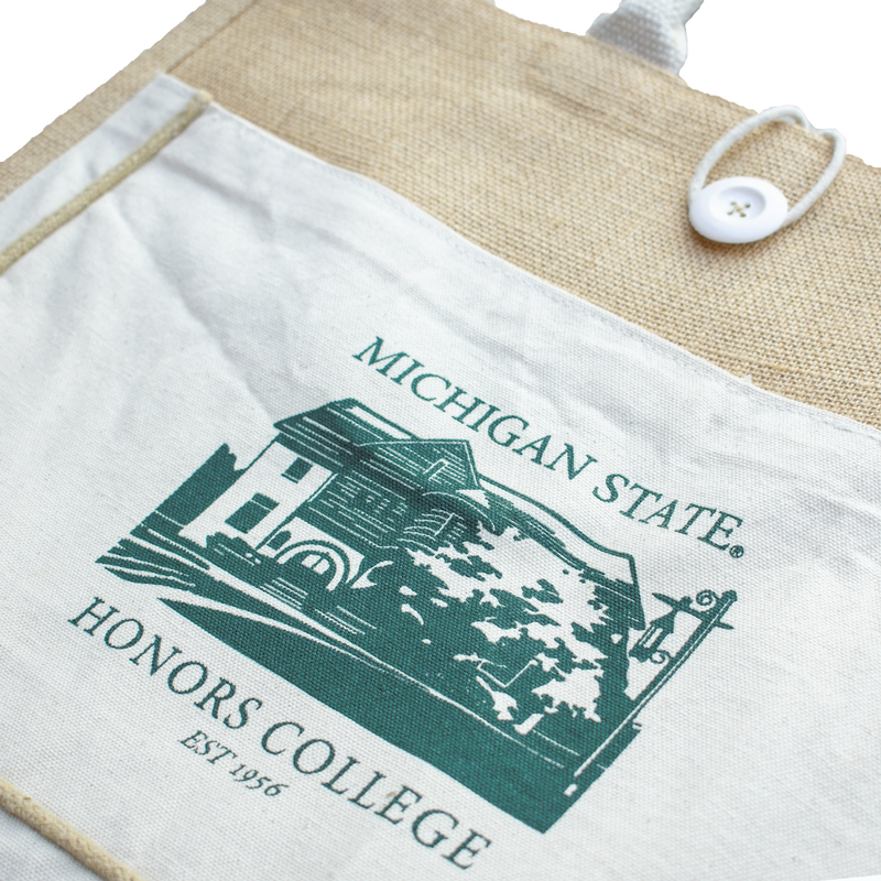 A tan and white tote bag made of jute and canvas material. On the side of the tote in green is a graphic of the Michigan State honors college. Above and below the image is the text "Michigan State Honors College Est. 1956"