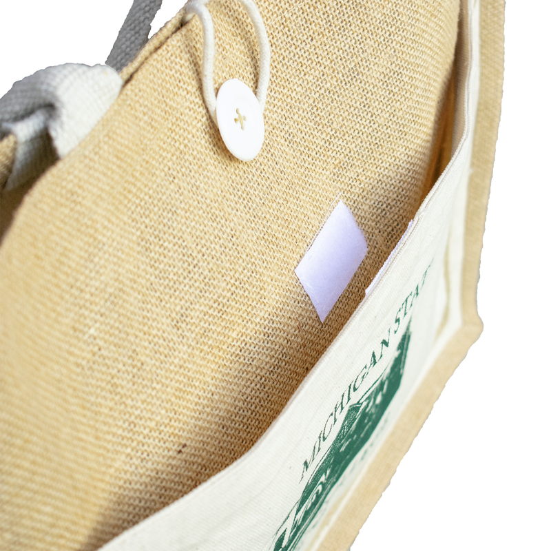 A tan and white tote bag made of jute and canvas material. On the side of the tote in green is a graphic of the Michigan State honors college. Above and below the image is the text "Michigan State Honors College Est. 1956"