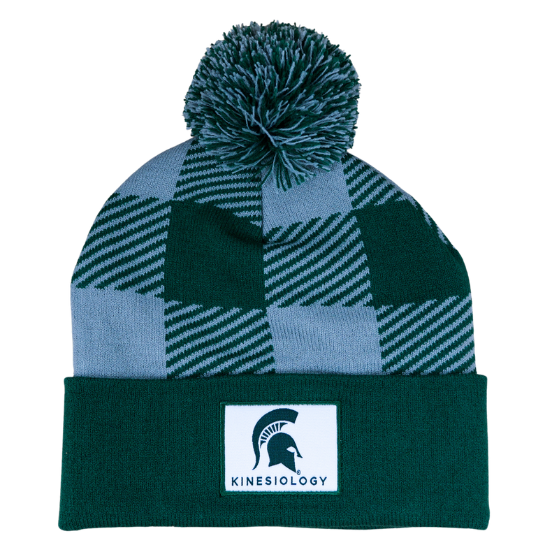 A green and gray plaid beanie with a matching pom. The cuff of the hat is an MSU green with a white sewn patch that features the MSU helmet with "Kinesiology" in green.