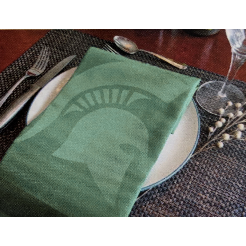 Green cloth napkin folded to show the slightly lighter Spartan helmet printing. Napkin is on a plate setting