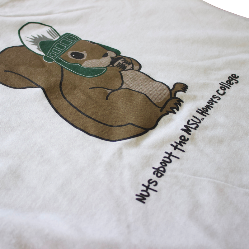 A white t-shirt with green trim on the collar and sleeves. The shirt features a cartoon image of a brown squirrel wearing a Spartan helmet. Below the squirrel, black text reads: "Nuts about the MSU Honors College." 