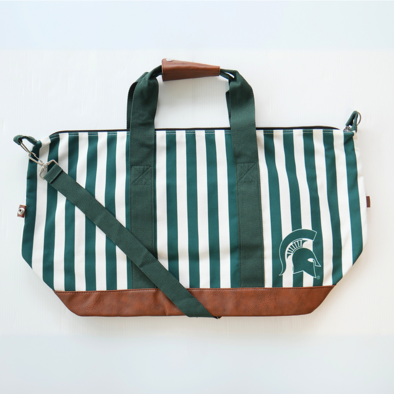 A green and white vertical striped canvas tote bag with a brown leather bottom and strap handles. The bag also has a green crossbody strap. In the lower right corner of the tote bag is a green MSU spartan helmet logo. 