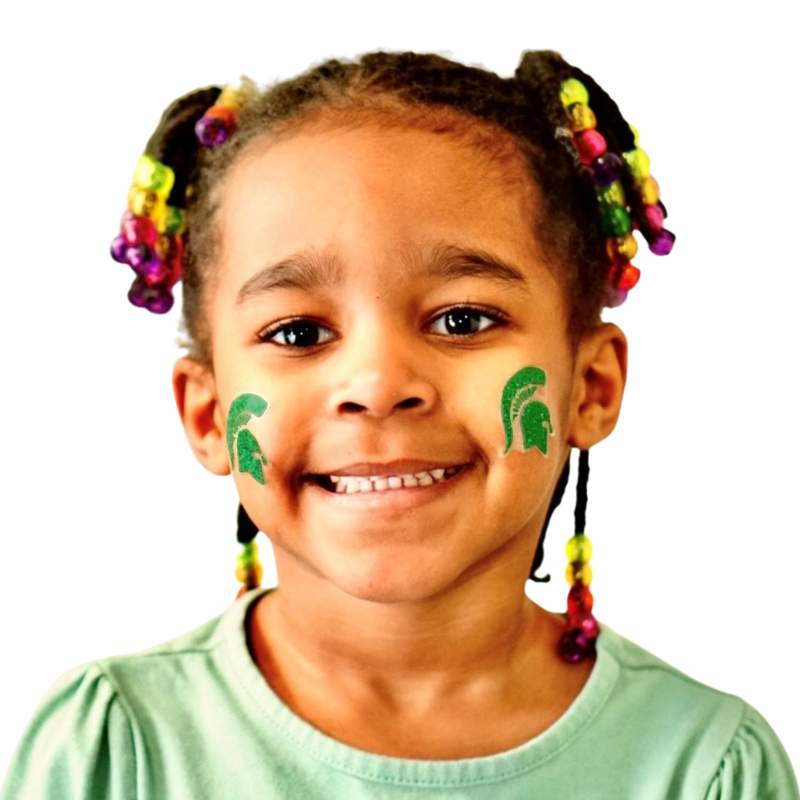 A little girl smiles broadly at the camera, sporting a glittery green Spartan helmet sticker on each cheek.