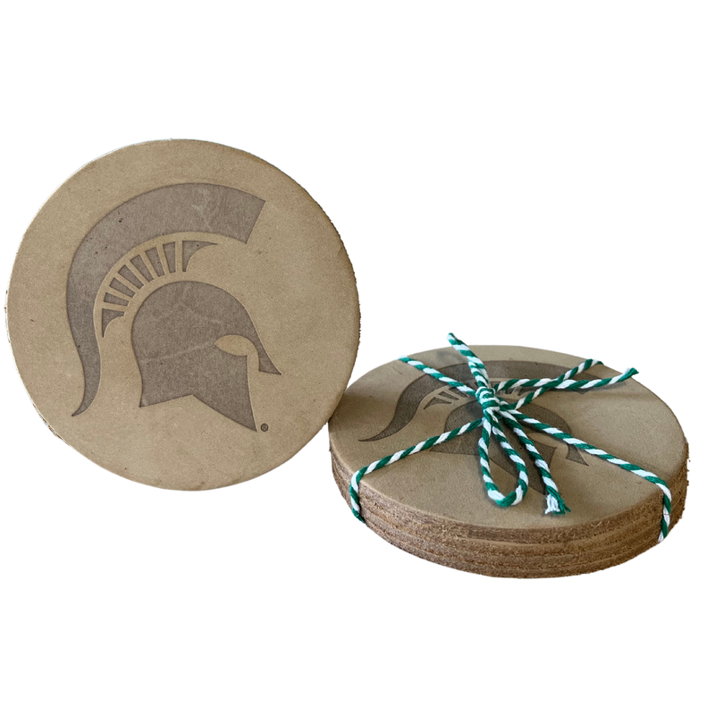Stack of four tan leather coasters with a large Spartan helmet embossed in the center of each. The stack is bound with green and white yarn ribbon.