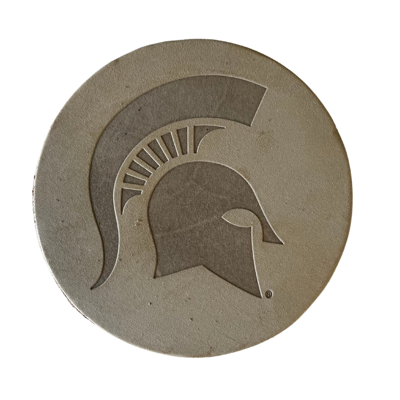 A tan leather coaster with a large Spartan helmet embossed in the center 