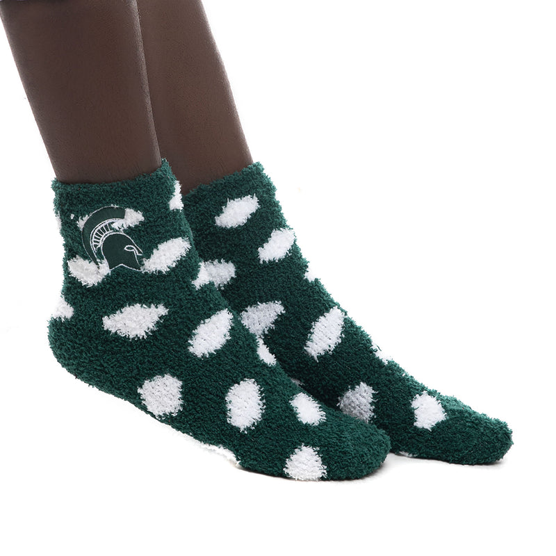 Closeup of  model's feet wearing fuzzy green ankle socks with large white polka dots and green Spartan helmet at ankle.