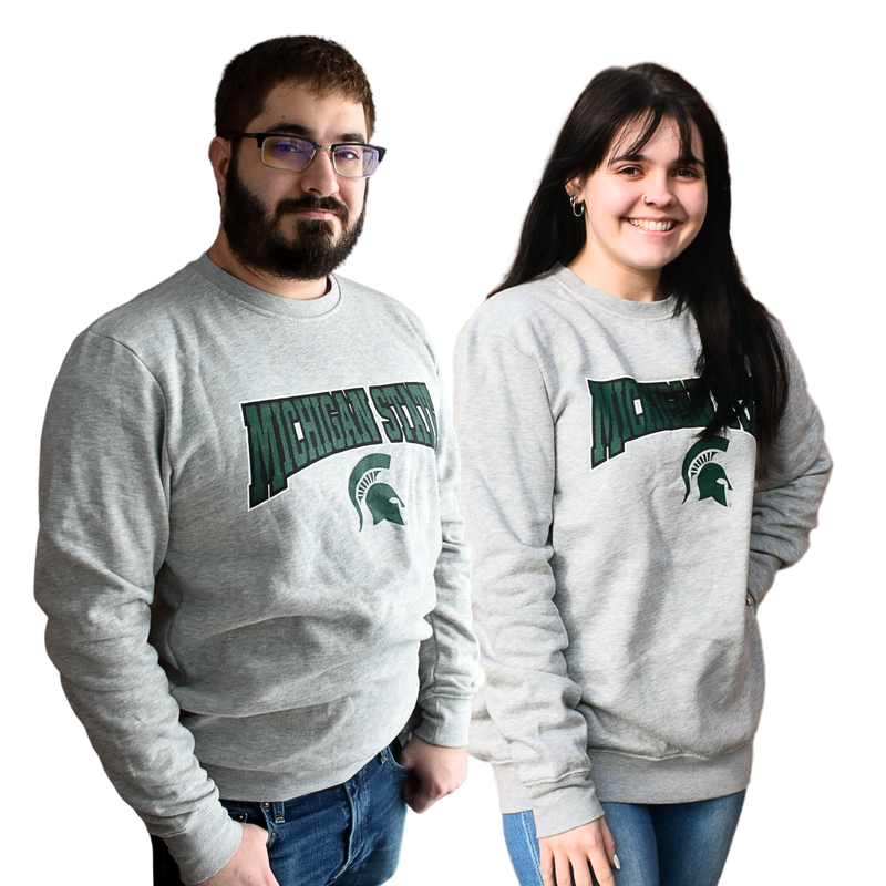 Man and woman standing side by side wearing a light heather gray crewneck sweatshirt, with Michigan State printed in a graphic arch over a Spartan helmet on the center chest.