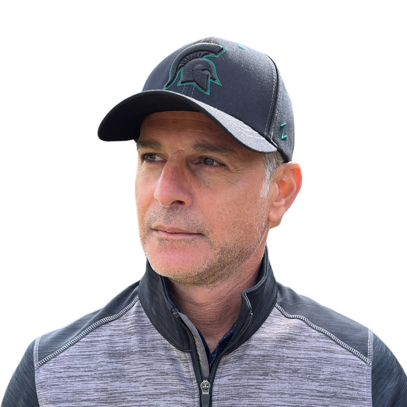 Man wearing a black baseball cap. On the front is a large embroidered black Spartan helmet that is outlined in green.