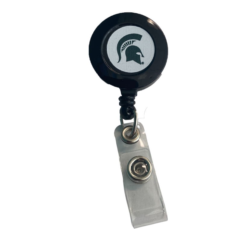 Circular black badge holder with a green Spartan helmet on a white background in its center. It is connected to a white snap strap tab with a metal fastener.
