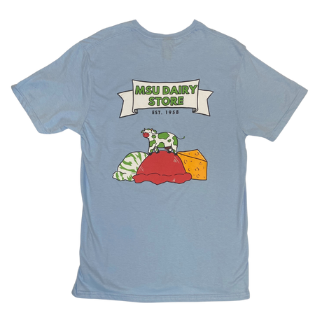 Back of a blue t-shirt with a large graphic on the back. Inside a white banner it reads MSU Dairy Store in green, and Est 1958 underneath. Below that is a cow with green spots standing on a red scoop of ice cream. To the left is a green and white scoop of ice cream and to the right is a wedge of orange cheese.