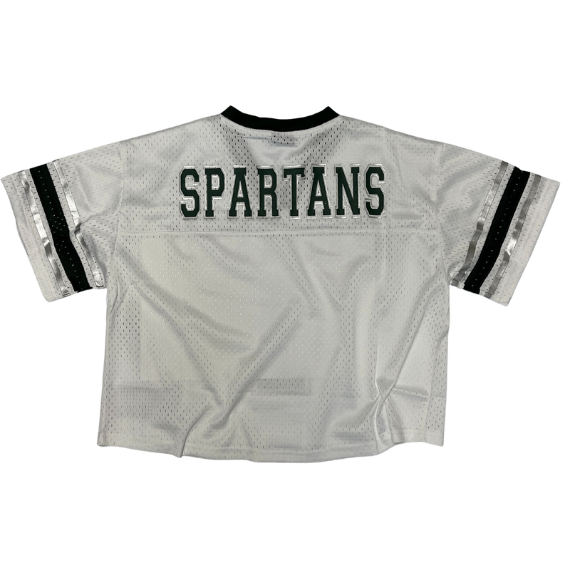 The back of a white, cropped Michigan State jersey with a green neckline and sleeve cuffs. Just below the neckline reads Spartans written in green in all caps. 