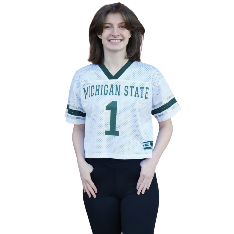 A woman wearing a white, cropped Michigan State jersey with a green neckline and sleeve cuffs. The torso has Michigan State written in all caps with the number one in green underneath.