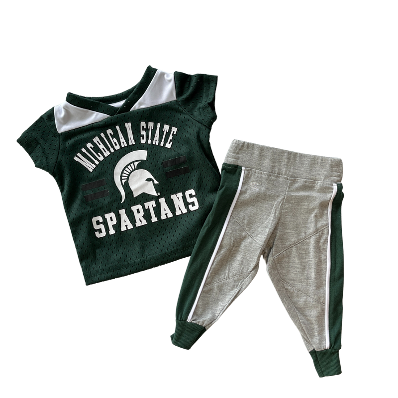A toddler or infant sized green football jersey with Michigan State Spartans and the MSU helmet logo written on the front. Grey sweatpants with green lines going down the side of the pant legs accompany the jersey. 