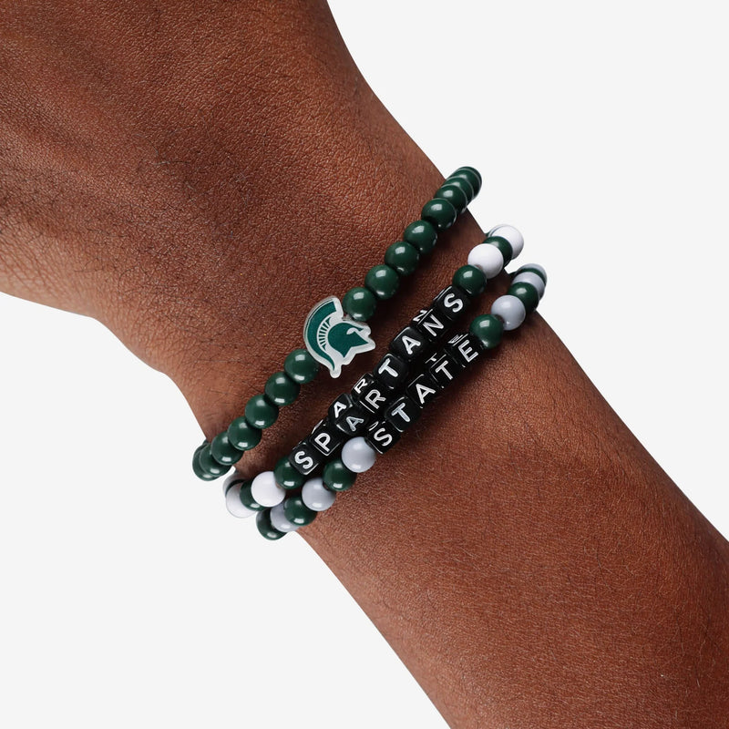 Three beaded bracelets on a man's wrist. Two are alternating green and white beads (one has Spartans the other has State in lettering), the third is all forest green. All three have a Spartan helmet charm, the all forest green bracelet one has two helmet charms.