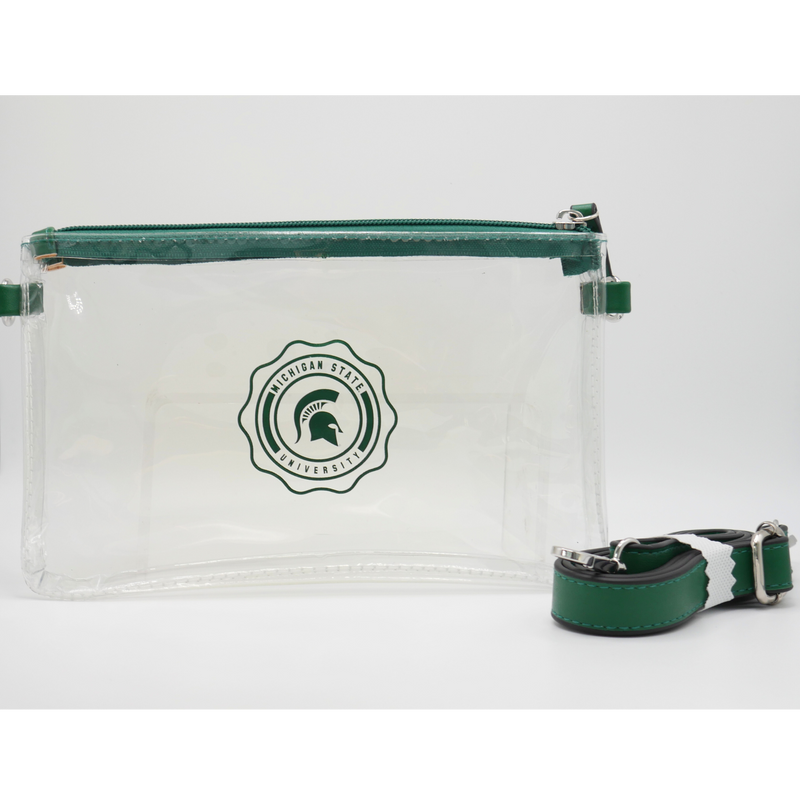 Clear rectangular pouch with green zipper. Decorative Michigan State University circle design printed on front. D-ring attachments on each side with green long crossbody strap. 