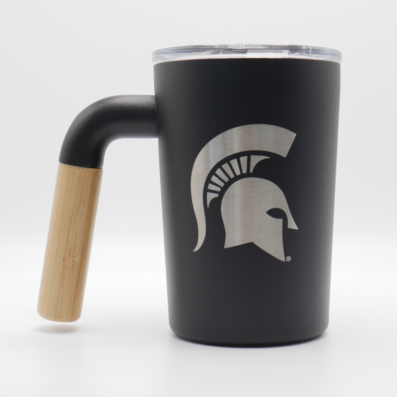 A black, 12 fluid ounce stainless steel coffee mug tumbler with a wooden handle. Engraved into the side of the tumbler in silver stainless steel is a Michigan State spartan helmet logo. 