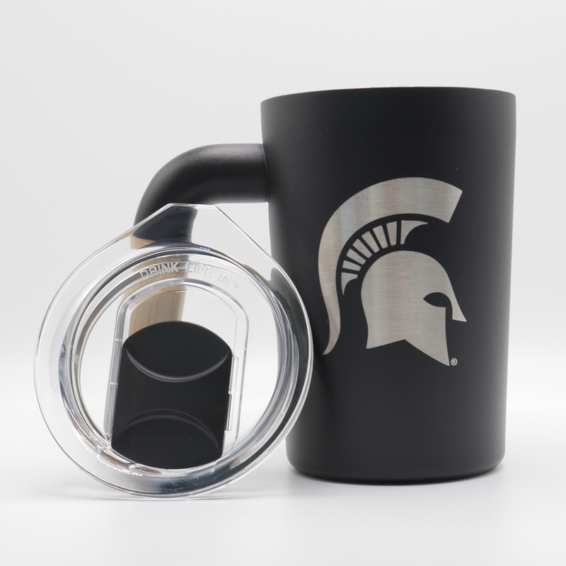 A black, 12 fluid ounce stainless steel coffee mug tumbler with a wooden handle. Engraved into the side of the tumbler in silver stainless steel is a Michigan State spartan helmet logo. The closable clear lid is displayed to the left of the tumbler. 