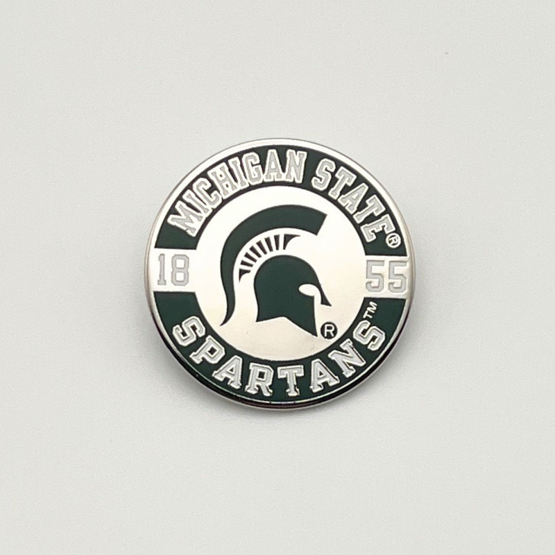 A round lapel pin with a silver color base. The pin has a green circle band around the outer edge with 'Michigan State SPARTANS' in white text. A green MSU spartan helmet logo is in the center, and a white 1855 to each side of the helmet logo. 