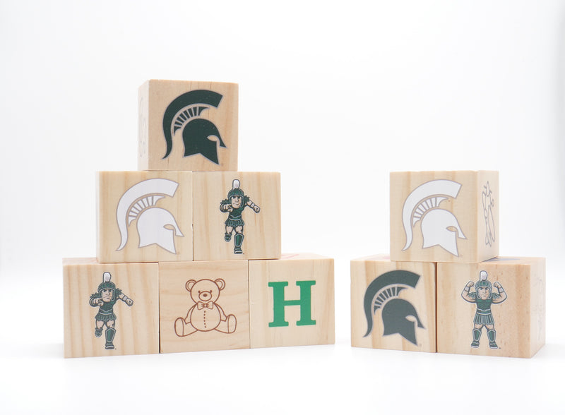 A set of nine wooden play block with various icons, letters, and numbers including Sparty and the MSU spartan helmet logo. 