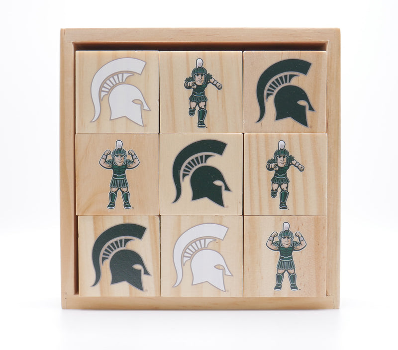 A set of nine wooden play blocks stacked 3 by 3 inside a wooden box. The blocks are showing various icons of Sparty and the MSU spartan helmet logo. 