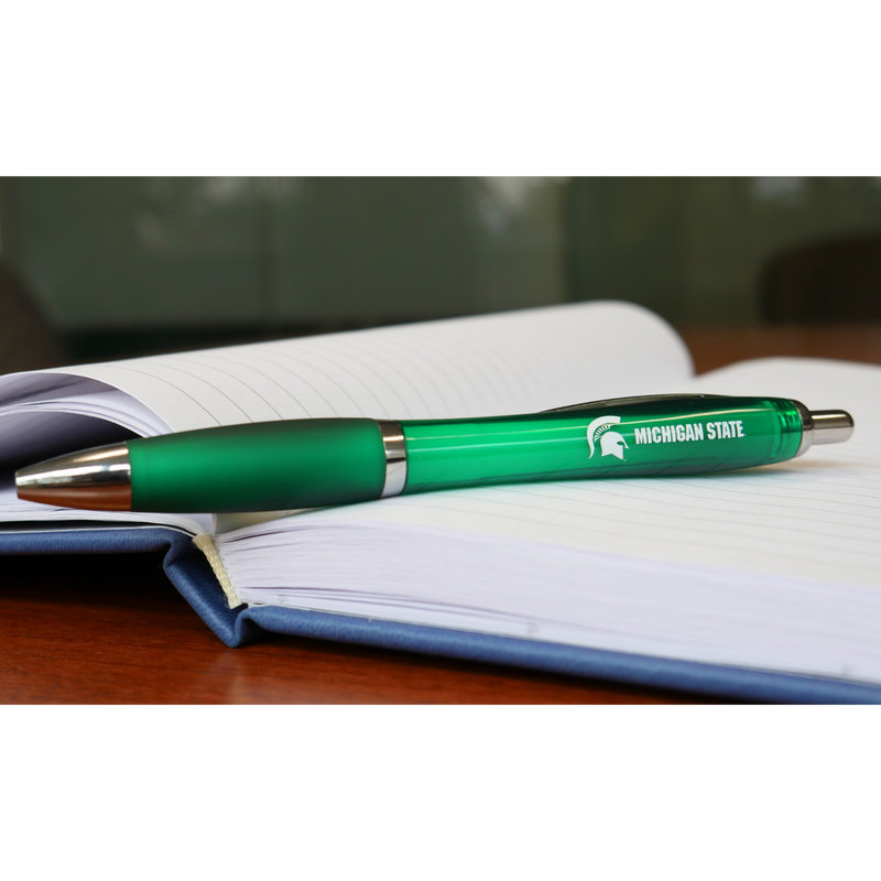 A green ballpoint pen. On the side of the pen, in white all caps text are the words "Michigan State". To the left of the text is a white MSU spartan helmet logo. The pen is sitting on top of an open business notebook. 