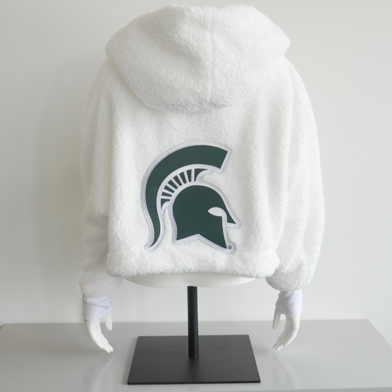 A white lounge jacket on a mannequin. On the back of the lounge jacket is a large green Michigan State University spartan helmet logo. 